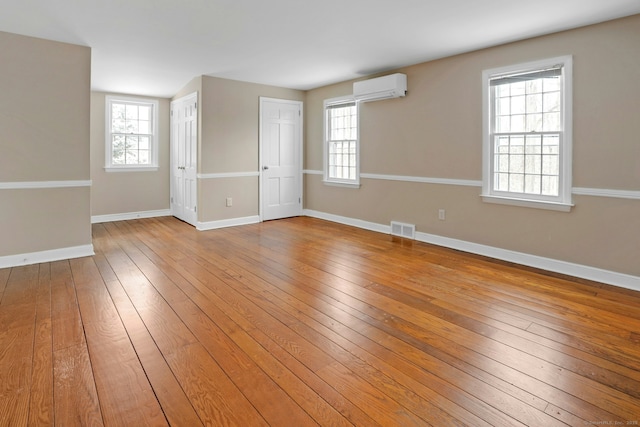 unfurnished room with a wall mounted AC, wood-type flooring, visible vents, and baseboards