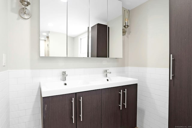 bathroom featuring a wainscoted wall, double vanity, a sink, and tile walls