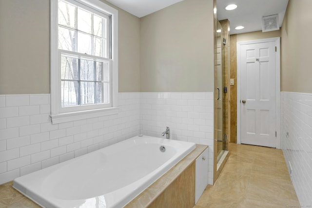 bathroom featuring tile walls, a stall shower, wainscoting, tile patterned flooring, and a bath