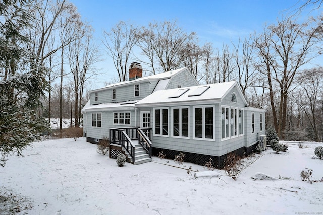 snow covered house with a garage, a sunroom, and a chimney