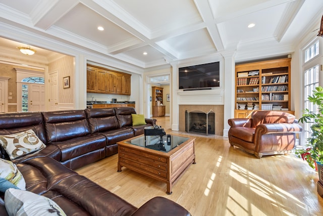 living room featuring beamed ceiling, ornamental molding, light hardwood / wood-style flooring, coffered ceiling, and a fireplace