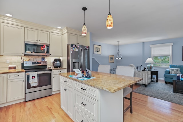 kitchen featuring appliances with stainless steel finishes, a kitchen breakfast bar, pendant lighting, light wood-type flooring, and a center island