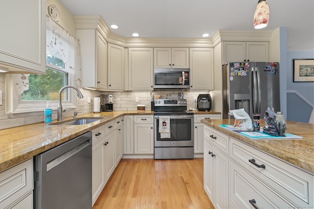 kitchen with light wood-type flooring, sink, tasteful backsplash, stainless steel appliances, and light stone countertops