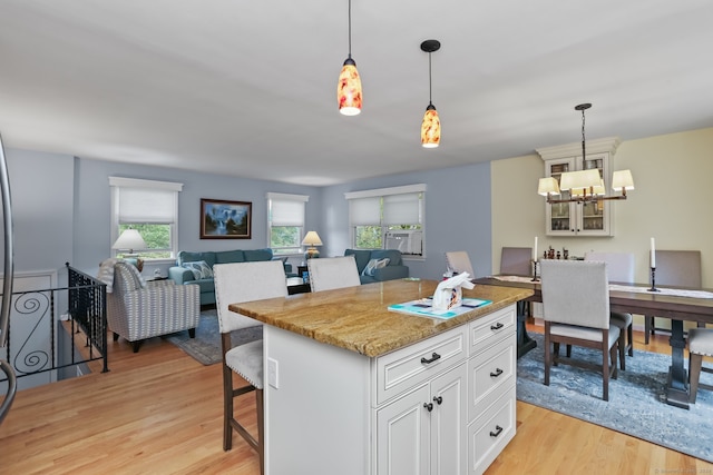 kitchen with light stone counters, hanging light fixtures, a kitchen island, a kitchen breakfast bar, and light wood-type flooring