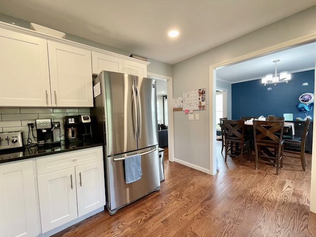 kitchen featuring ornamental molding, wood-type flooring, white cabinetry, stainless steel refrigerator, and decorative backsplash