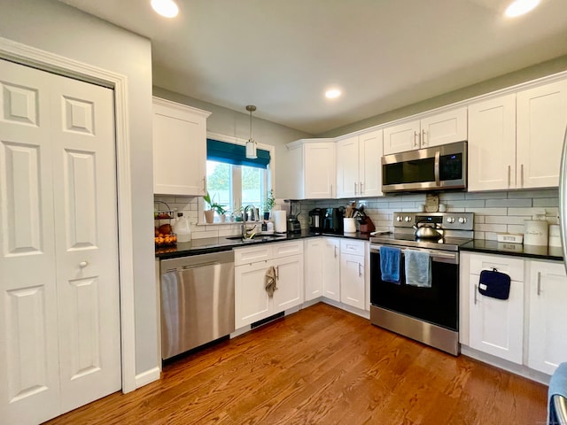 kitchen with stainless steel appliances, white cabinets, hardwood / wood-style flooring, sink, and hanging light fixtures