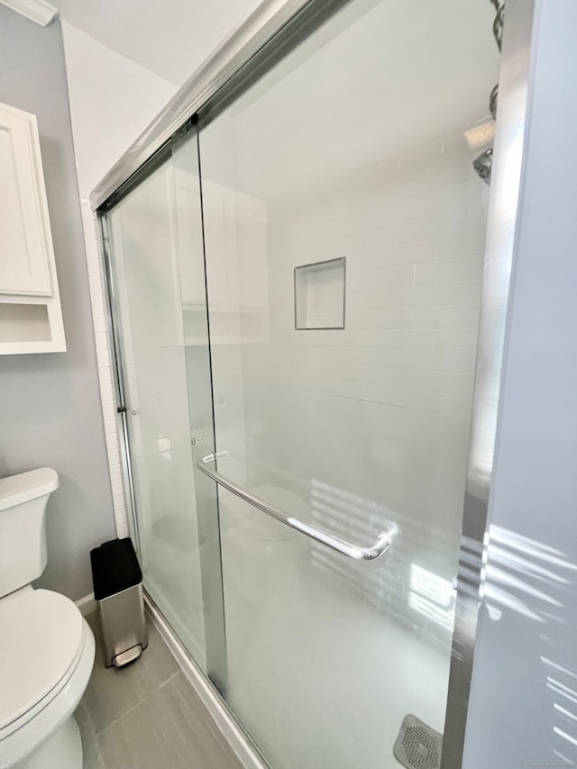 bathroom featuring tile patterned floors, a shower with door, and toilet