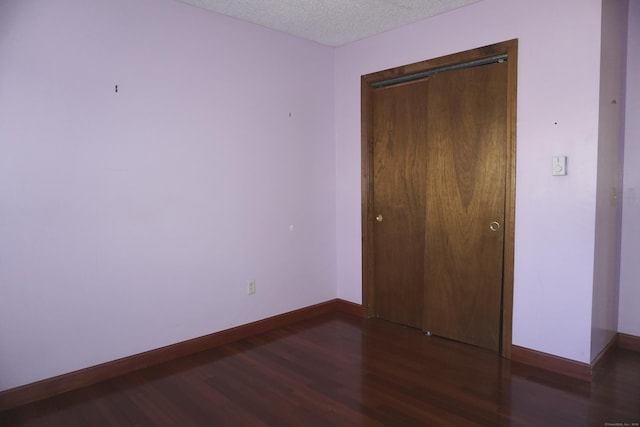 unfurnished bedroom featuring a textured ceiling, a closet, and dark hardwood / wood-style floors