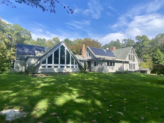 rear view of property with a yard, solar panels, and a chimney