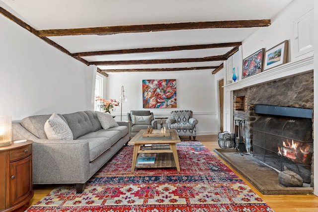 living room featuring a stone fireplace, beamed ceiling, and hardwood / wood-style floors