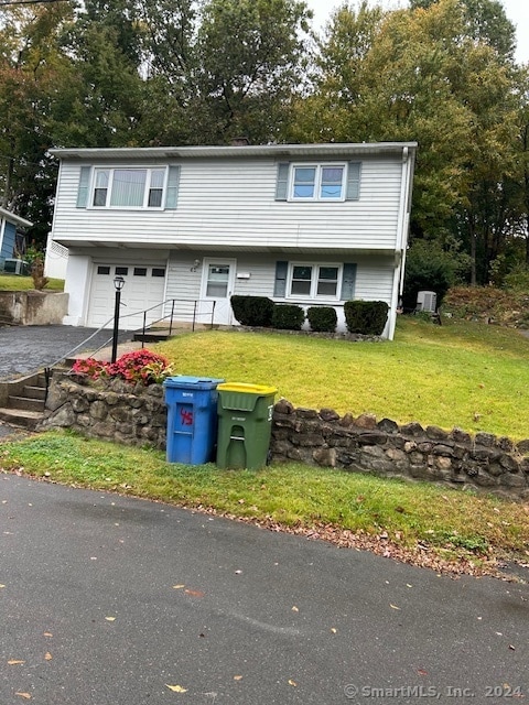 view of front of property with a front yard, a garage, and central AC unit