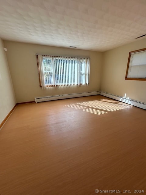 empty room with a baseboard heating unit, light hardwood / wood-style floors, and a textured ceiling