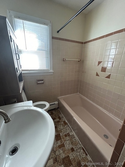 full bathroom with toilet, baseboard heating, sink, tile walls, and tiled shower / bath