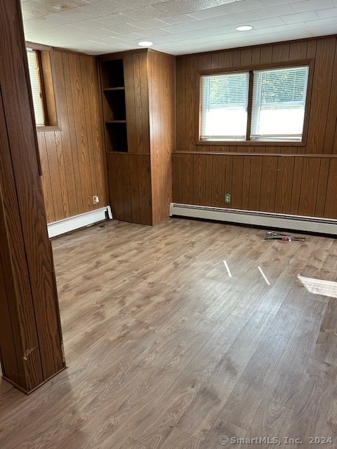 spare room with wood walls, wood-type flooring, and a baseboard heating unit