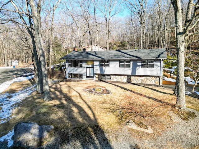 raised ranch featuring stone siding, a chimney, and a forest view