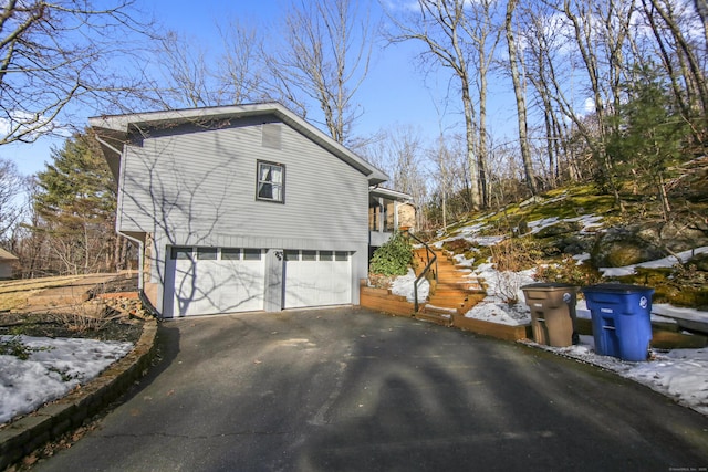 view of side of property featuring aphalt driveway, an attached garage, and stairs