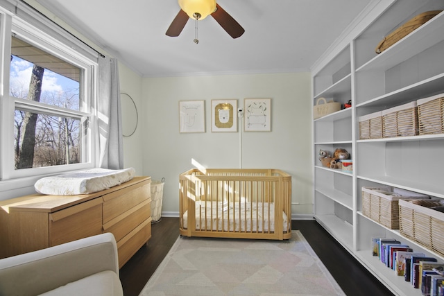 bedroom with crown molding, ceiling fan, baseboards, wood finished floors, and a nursery area