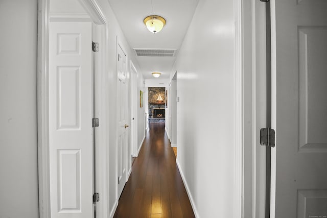 hallway with dark wood finished floors, visible vents, and baseboards