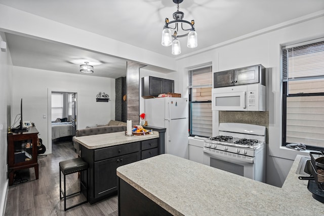 kitchen featuring pendant lighting, white appliances, dark hardwood / wood-style floors, a notable chandelier, and a kitchen bar