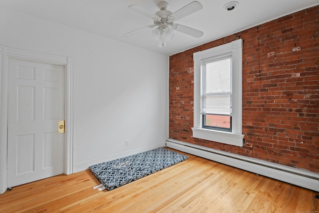 spare room featuring ceiling fan, hardwood / wood-style flooring, baseboard heating, and brick wall