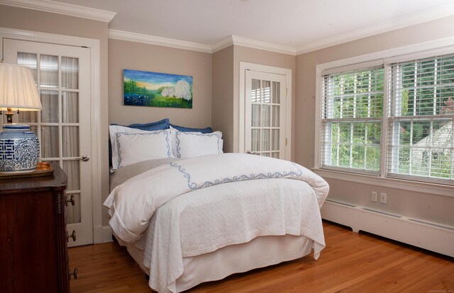 bedroom with a baseboard radiator, hardwood / wood-style flooring, and crown molding