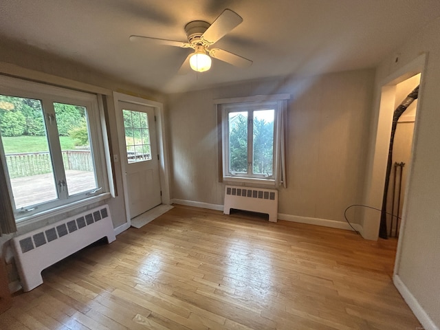 additional living space with light wood-type flooring, a healthy amount of sunlight, and radiator heating unit