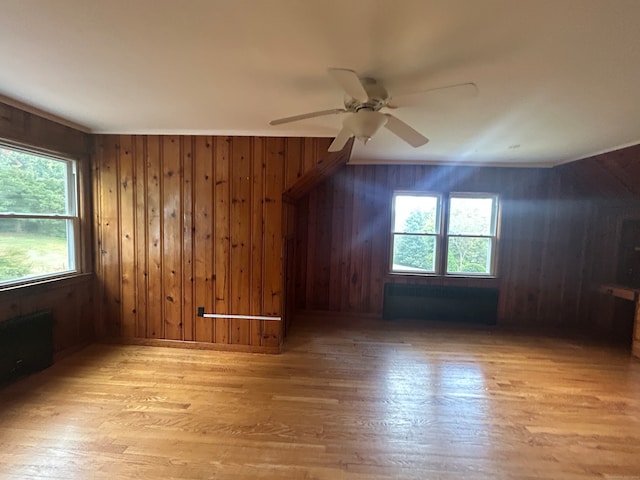 additional living space with light hardwood / wood-style flooring, wooden walls, ceiling fan, and a healthy amount of sunlight