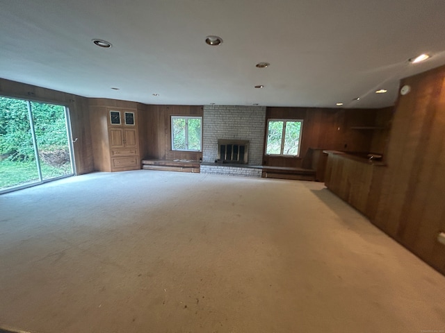 unfurnished living room with light carpet, wooden walls, a brick fireplace, and a healthy amount of sunlight