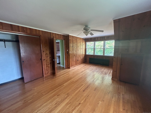 unfurnished bedroom with light wood-type flooring, wood walls, ornamental molding, and ceiling fan