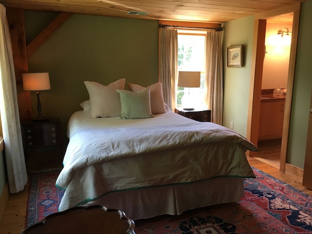 bedroom featuring wooden ceiling, hardwood / wood-style flooring, and ensuite bath