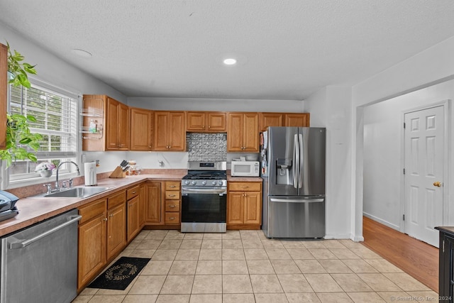 kitchen with tasteful backsplash, a textured ceiling, stainless steel appliances, sink, and light tile patterned floors