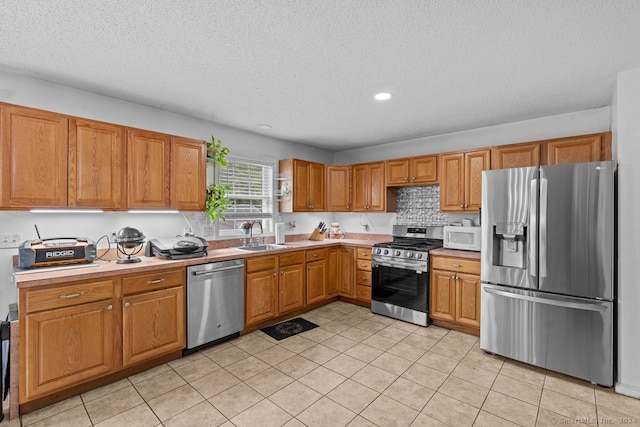 kitchen featuring sink, light tile patterned floors, a textured ceiling, appliances with stainless steel finishes, and tasteful backsplash