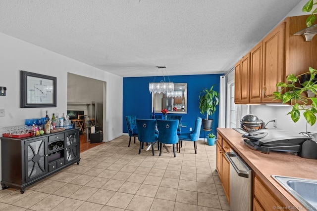 kitchen with stainless steel dishwasher, a textured ceiling, pendant lighting, light tile patterned floors, and an inviting chandelier