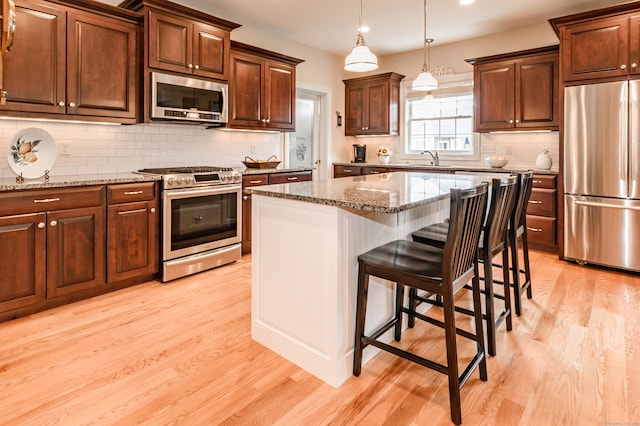 kitchen with light stone countertops, a center island, appliances with stainless steel finishes, and light hardwood / wood-style floors