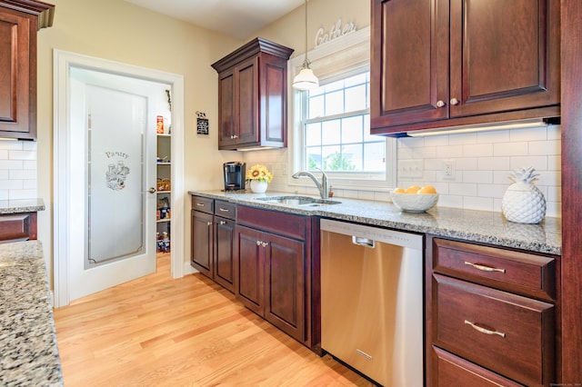 kitchen featuring hanging light fixtures, sink, light wood-type flooring, stainless steel dishwasher, and light stone counters