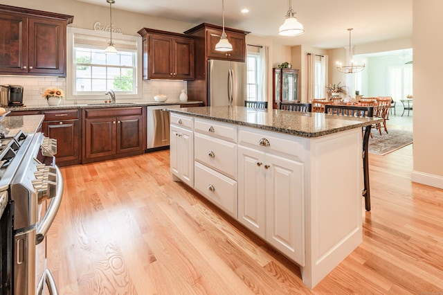 kitchen with white cabinets, hanging light fixtures, appliances with stainless steel finishes, light hardwood / wood-style flooring, and sink