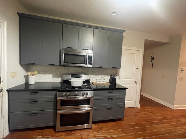 kitchen featuring appliances with stainless steel finishes, gray cabinets, dark wood-type flooring, and tasteful backsplash