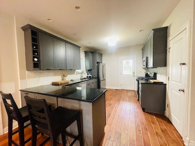 kitchen with sink, kitchen peninsula, backsplash, appliances with stainless steel finishes, and light wood-type flooring