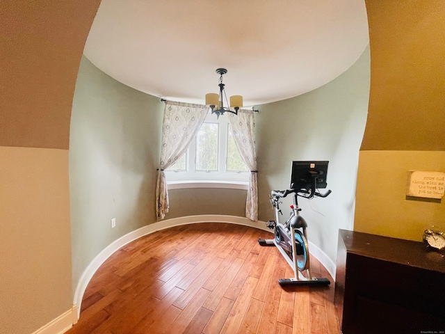 exercise area with wood-type flooring and a notable chandelier