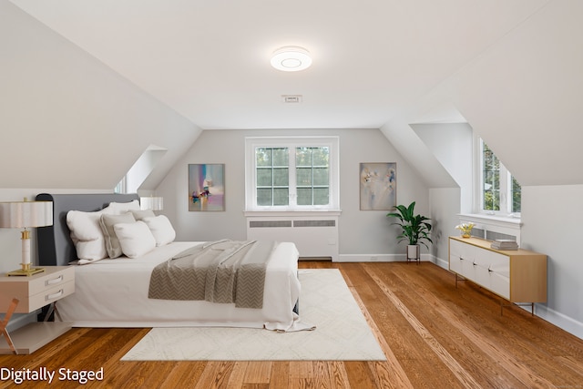 bedroom with multiple windows, lofted ceiling, radiator, and light hardwood / wood-style flooring