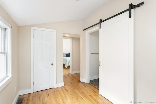 unfurnished bedroom featuring light hardwood / wood-style flooring, a barn door, and vaulted ceiling