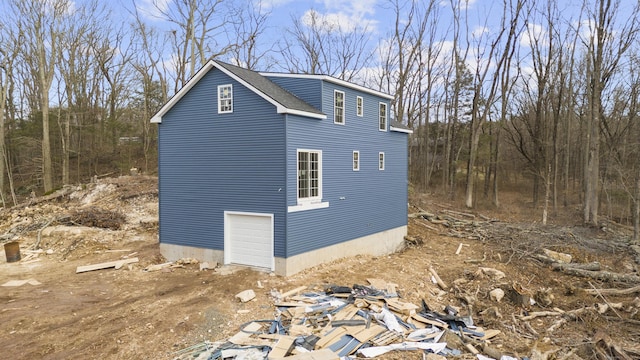 view of side of property with roof with shingles, an attached garage, and dirt driveway