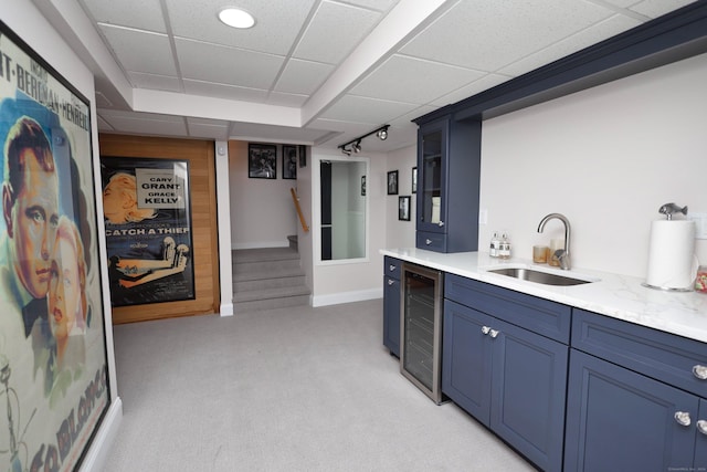 bar featuring a paneled ceiling, light carpet, sink, blue cabinetry, and beverage cooler