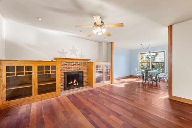 unfurnished living room with a brick fireplace, ceiling fan with notable chandelier, and hardwood / wood-style floors