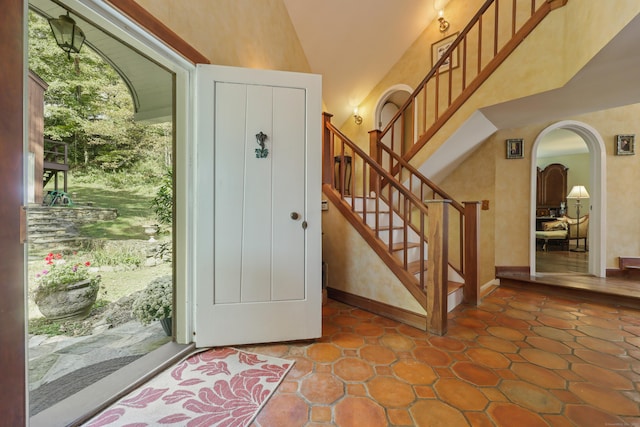 foyer with arched walkways, high vaulted ceiling, stairway, and baseboards