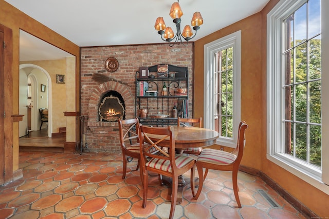 dining room featuring arched walkways, a fireplace, visible vents, a chandelier, and baseboards