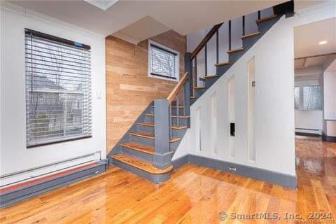 staircase featuring wooden walls, hardwood / wood-style floors, and a baseboard heating unit