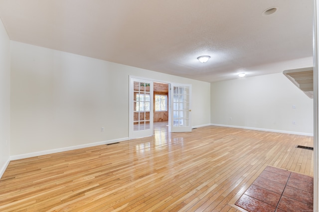 unfurnished room with french doors, a textured ceiling, and light wood-type flooring