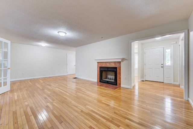 unfurnished living room with a textured ceiling, light wood-type flooring, and a tile fireplace