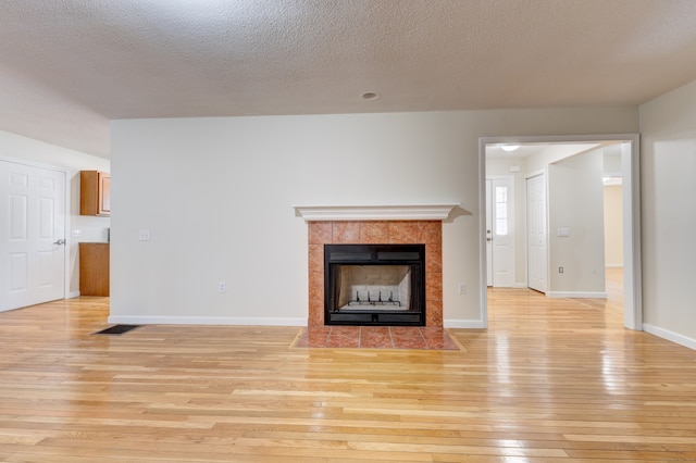 unfurnished living room with light wood-type flooring, a tile fireplace, and a textured ceiling